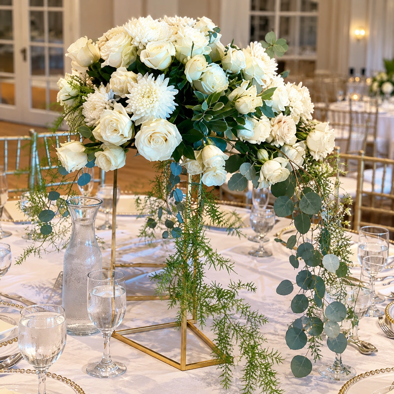 Ivory wedding centerpiece on a gold stand with cascading greenery